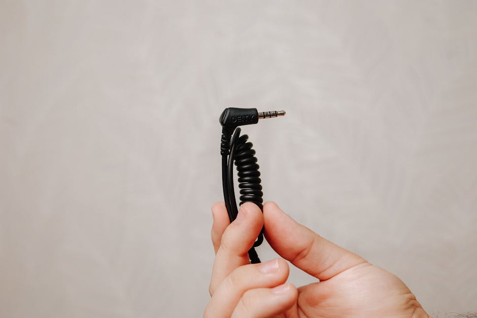 Closeup of a hand holding a coiled audio cable plug against a neutral background.