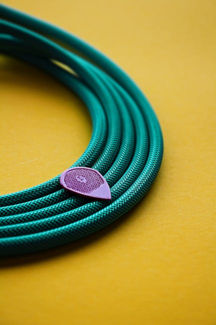 A close-up shot of a green instrument cable and a purple guitar pick against a yellow background, ideal for music equipment themes.