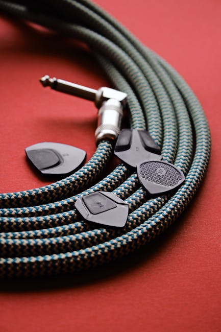 Close-up of a braided guitar cable and picks on a vibrant red surface.