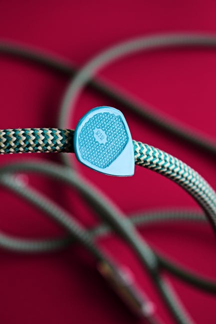 Detailed view of a guitar pick resting on a colorful braided cable against a red background.