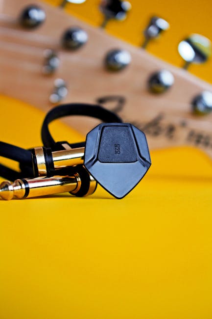 Guitar cable and pick on vibrant yellow backdrop, perfect for music themes.