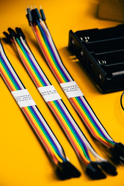 Vibrant close-up of rainbow-colored jumper wires and a battery holder on a yellow background.