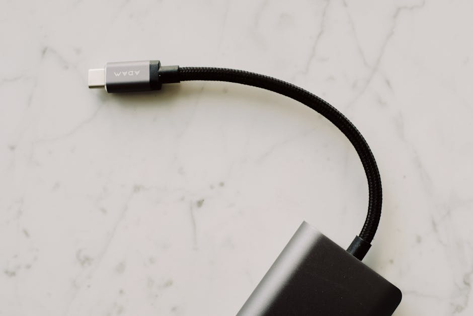 A close-up view of a black USB-C cable with a braided cord resting on a light marble surface. A close-up view of a black USB-C cable with a braided cord resting on a light marble surface.