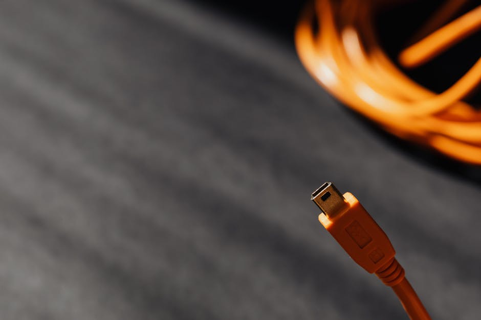 Macro shot of an orange USB cable connector on a textured surface with soft shadows.