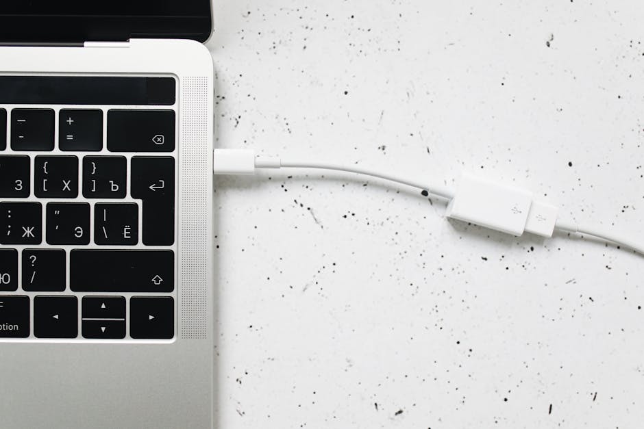 Close-up of a USB cable connected to a laptop keyboard on a white textured surface.