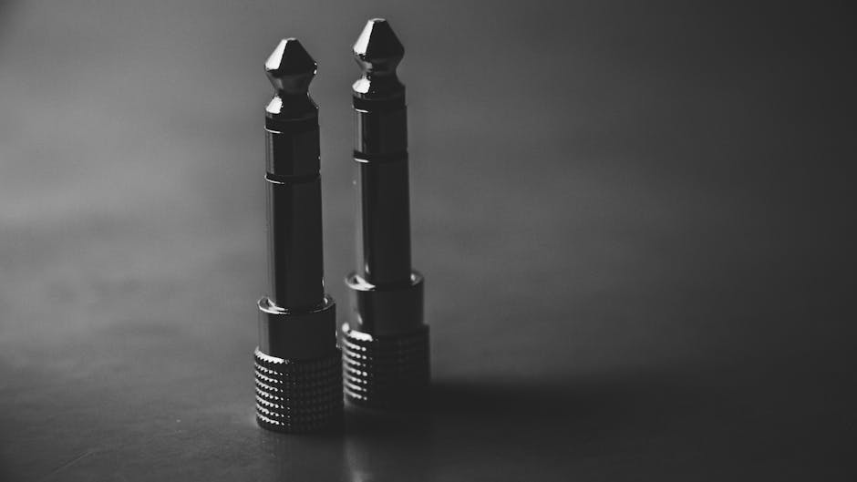 Black and white close-up of two audio jack plugs in a studio setting.