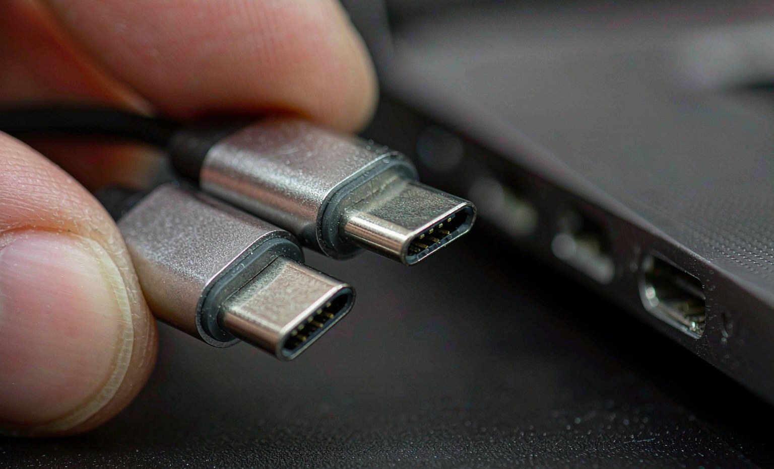 Close-up of two USB Type-C connectors held beside a laptop port